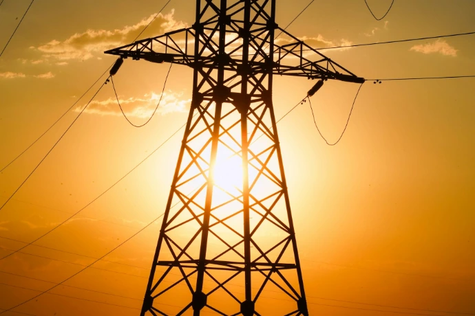An electric tower stands silhouetted against the sunset